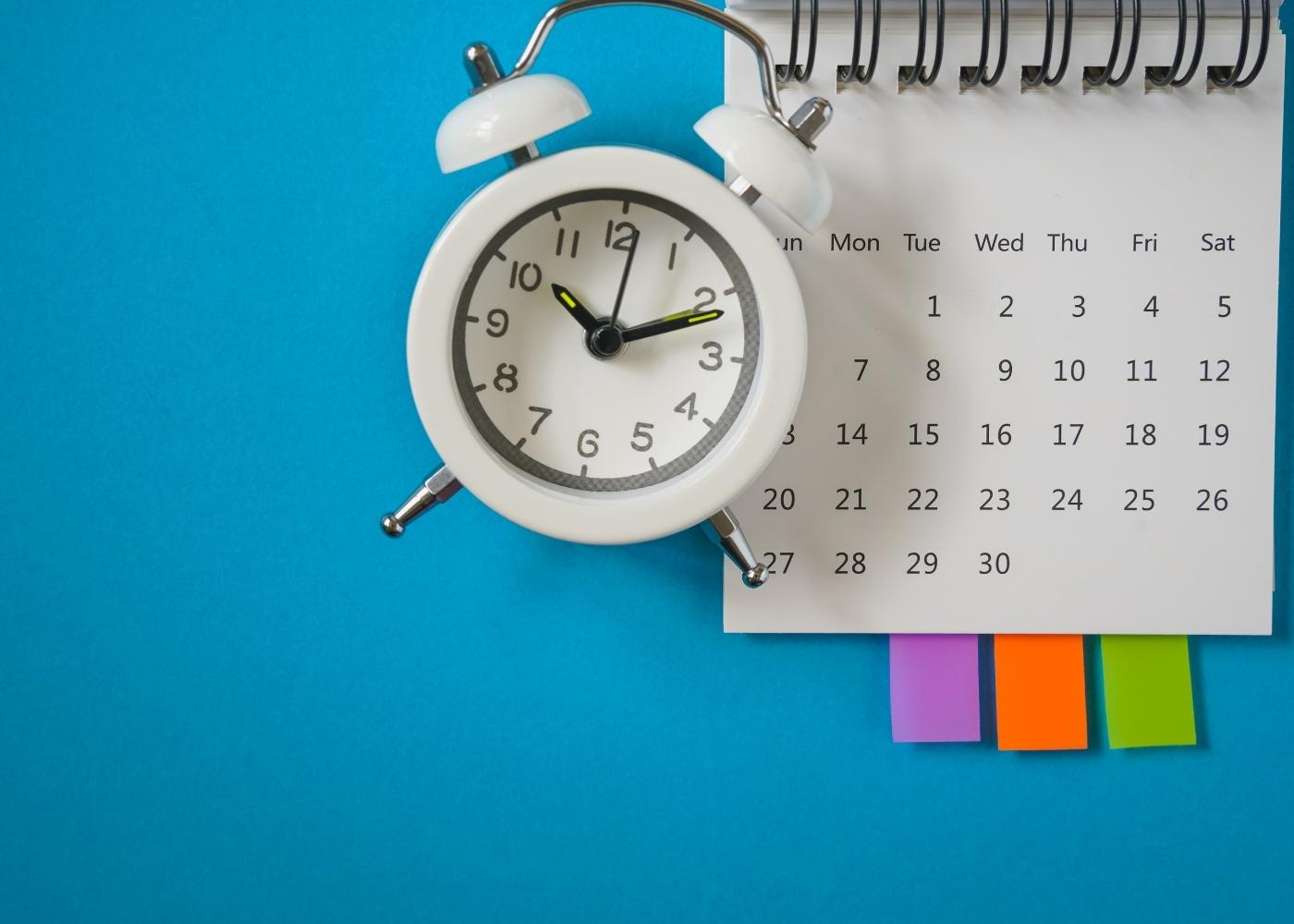white alarm clock and calendar on blue background